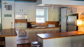 A kitchen with white cabinets, a stove, a sink, and a refrigerator.
