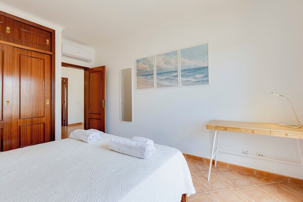 A bedroom with a bed, a wooden wardrobe, a desk, and a beach painting on the wall. - Spacious Villa - Walk to Beach & City Center (Lagos)