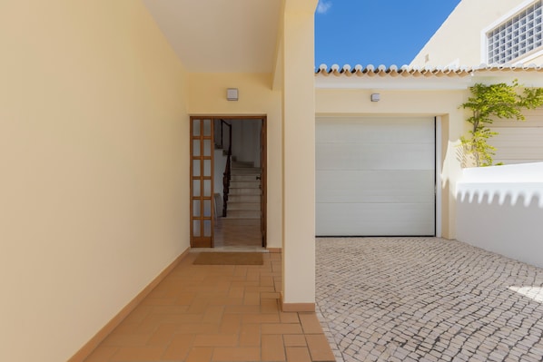 A narrow hallway with a tiled floor, a closed garage door, and a staircase leading to an upper level. - Spacious Villa - Walk to Beach & City Center (Lagos)