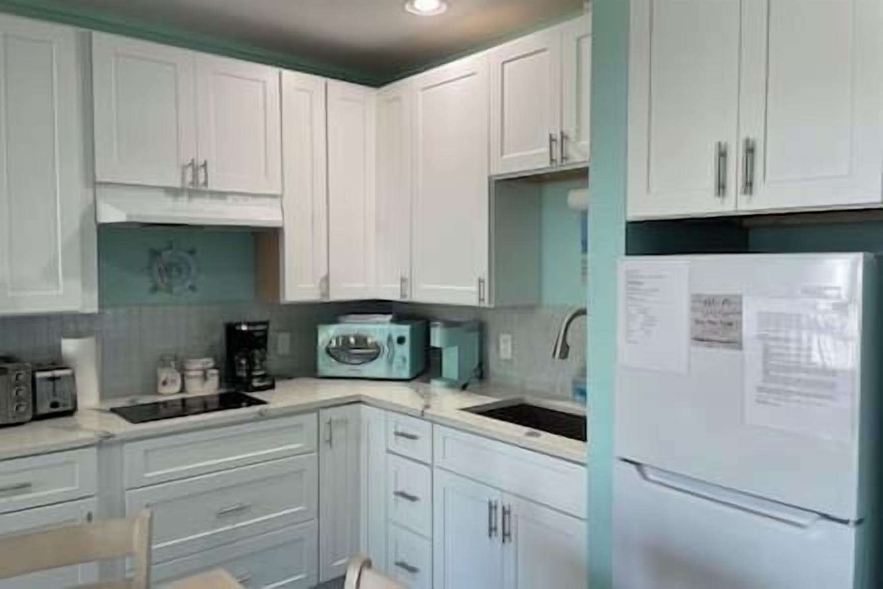 A kitchen with white cabinets, a microwave, a coffee maker, and a refrigerator.