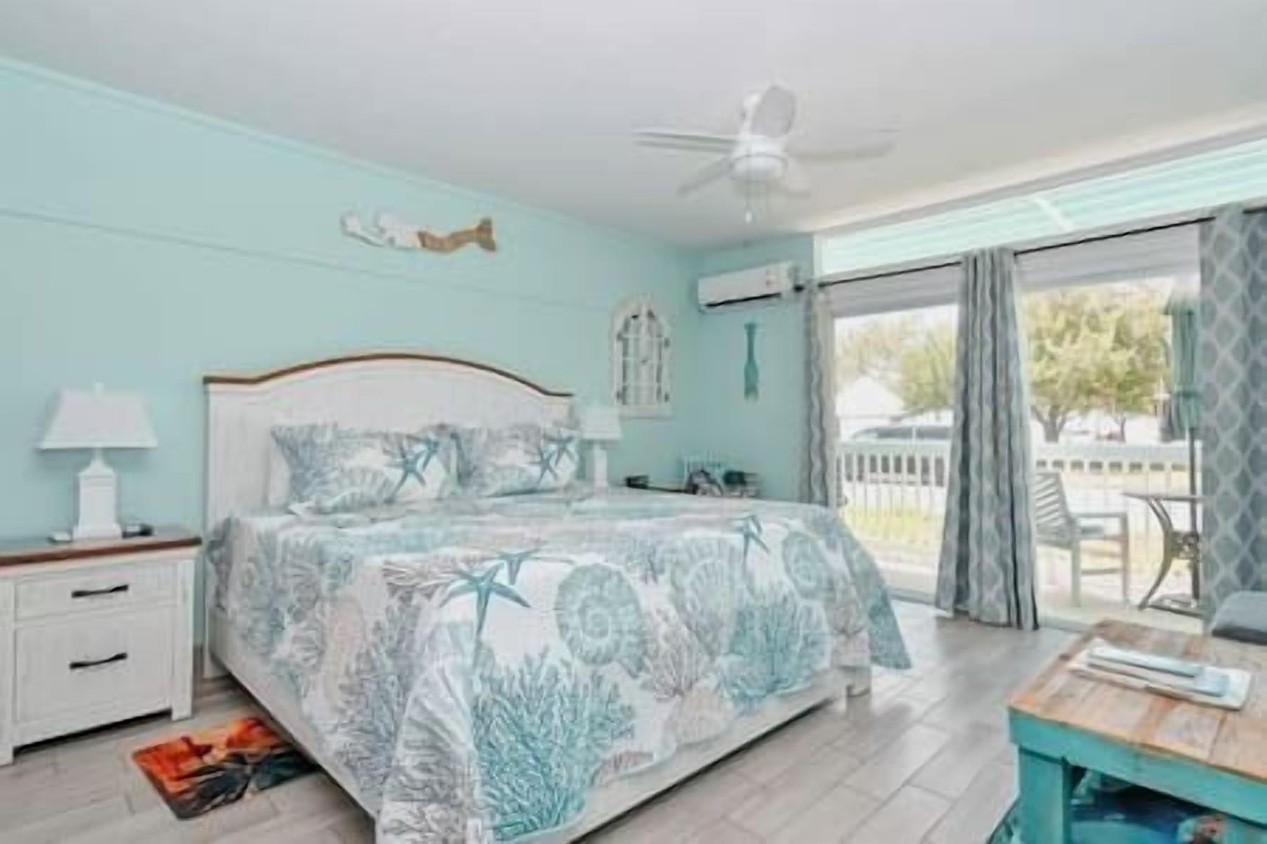 A bedroom with a bed, a nightstand, a lamp, a ceiling fan, and a view of the outdoors.