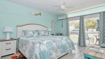 A bedroom with a bed, a nightstand, a lamp, a ceiling fan, and a view of the outdoors.
