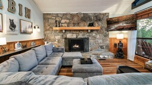 Una sala de estar acogedora con una chimenea de piedra, un sofá seccional gris grande y una mesa de centro de madera.