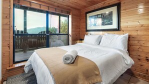 Una habitación con paneles de madera, una cama, un ventanal grande y un cuadro en la pared.