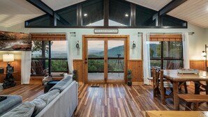 Amplia sala de estar con techo alto, piso de madera y un ventanal con vistas a un paisaje pintoresco.