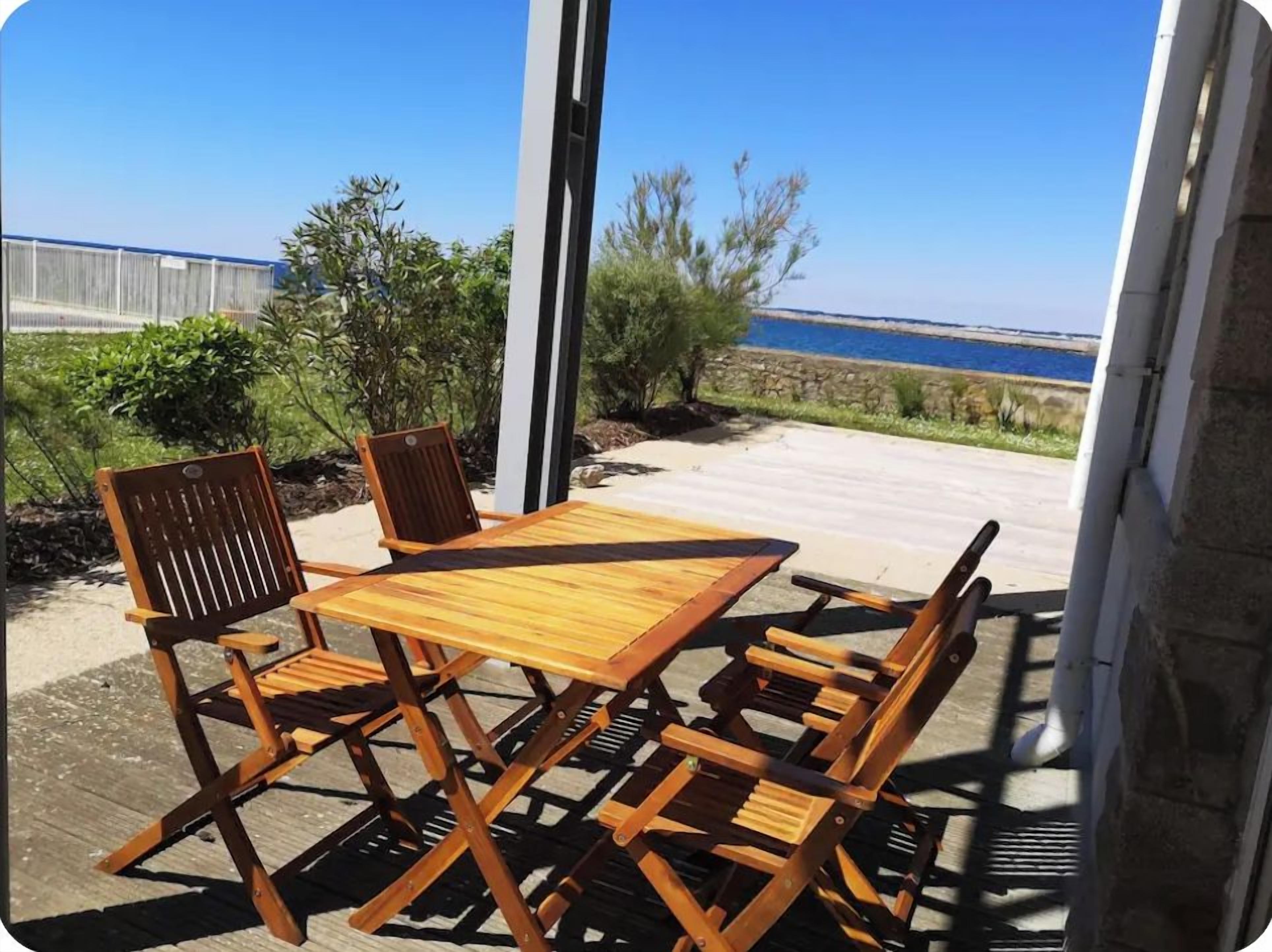 Une terrasse en bois avec une table et des chaises, donnant sur une étendue d’eau et bordée d’une clôture.