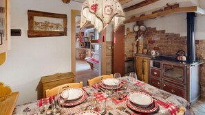 A rustic dining area with a wooden table set for four, a hanging chandelier, and a stone fireplace in the background.