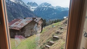 A window with a view of a rustic wooden cabin and snow-capped mountains.