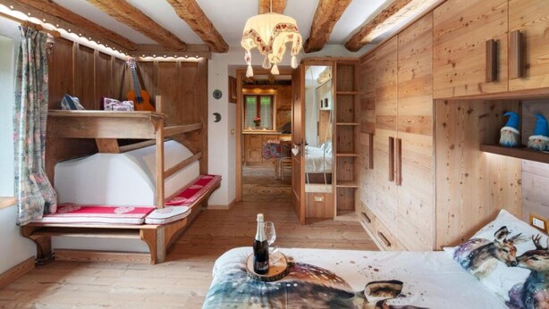 A rustic wooden room with a bunk bed, a small table with a bottle, and a bed with a deer print pillow.