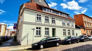 A two-story building with a white facade and a red-tiled roof. There are parked cars in front, and a street sign is visible. - Altstadtfreude Stralsund 5 (Stralsund)