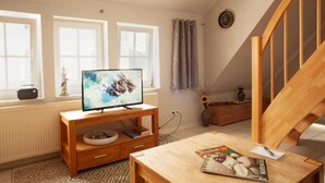 A modern living room with a television on a wooden stand, a coffee table with magazines, and a staircase. - Altstadtfreude Stralsund 5 (Stralsund)