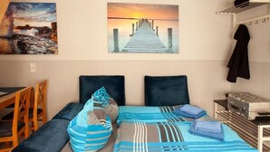 A bedroom with a bed, pillows, a blanket, a suitcase, and a painting of a sunset over a pier. - Altstadtfreude Stralsund 5 (Stralsund)