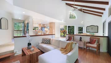A modern living room with a white sofa, wooden coffee table, and a view of the kitchen and outdoor area.