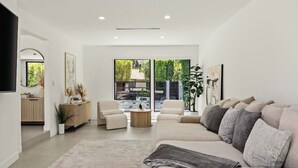 A modern living room with a beige sofa, a coffee table, and a large window offering a view of the outdoors.