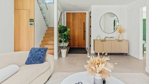 A modern living room with a sofa, a coffee table with a vase, a staircase, a wooden door, and a mirror on the wall.