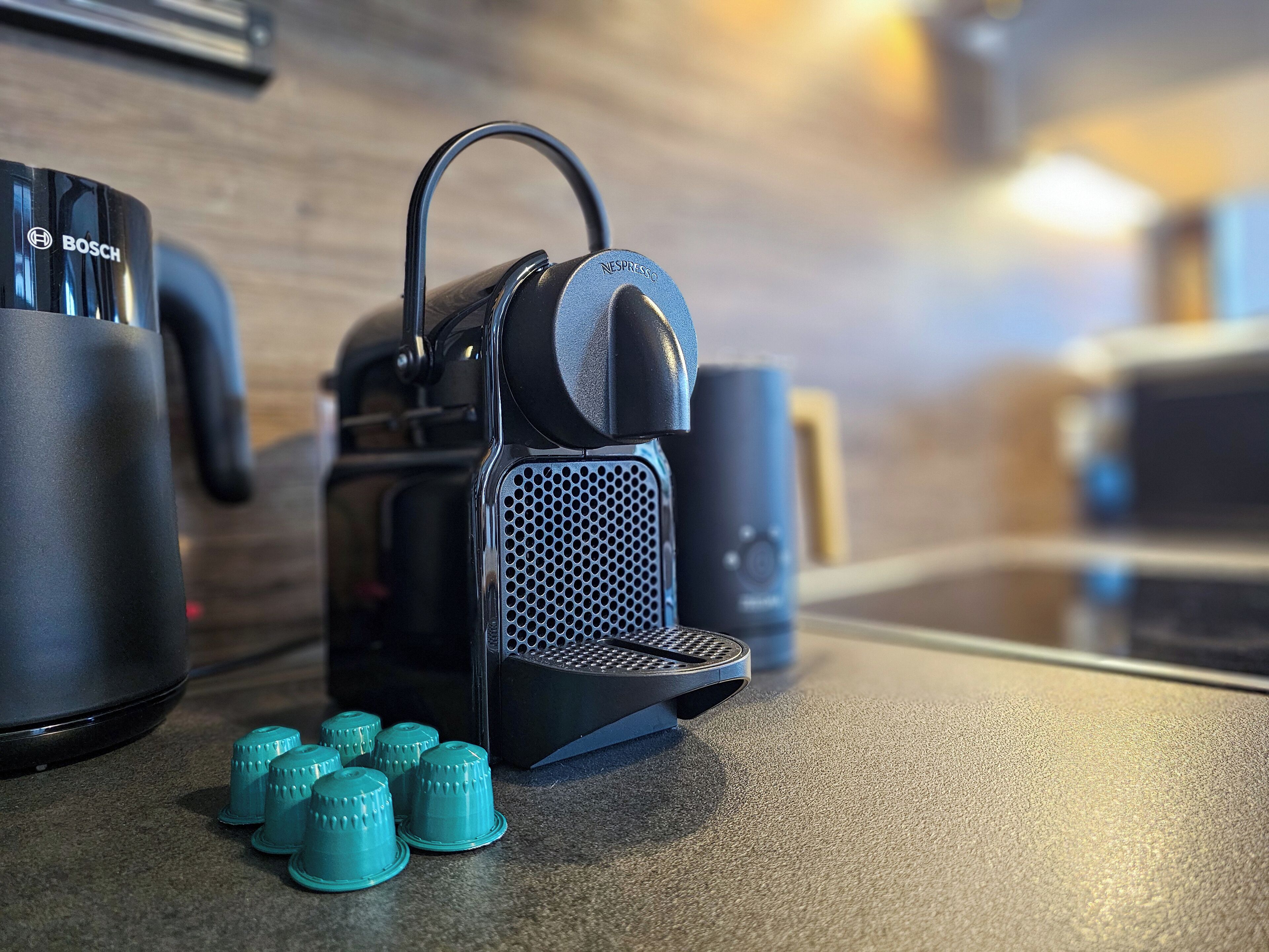 A kitchen with a Bosch coffee maker, a Nespresso machine, and several teal coffee capsules on the counter.