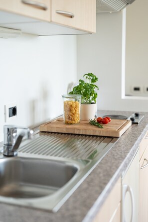 A kitchen with a sink, a cutting board with pasta, a potted basil plant, and a small herb sprig.