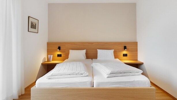 A double bed with a wooden headboard, two bedside tables with wall-mounted lamps, and a framed picture on the wall.