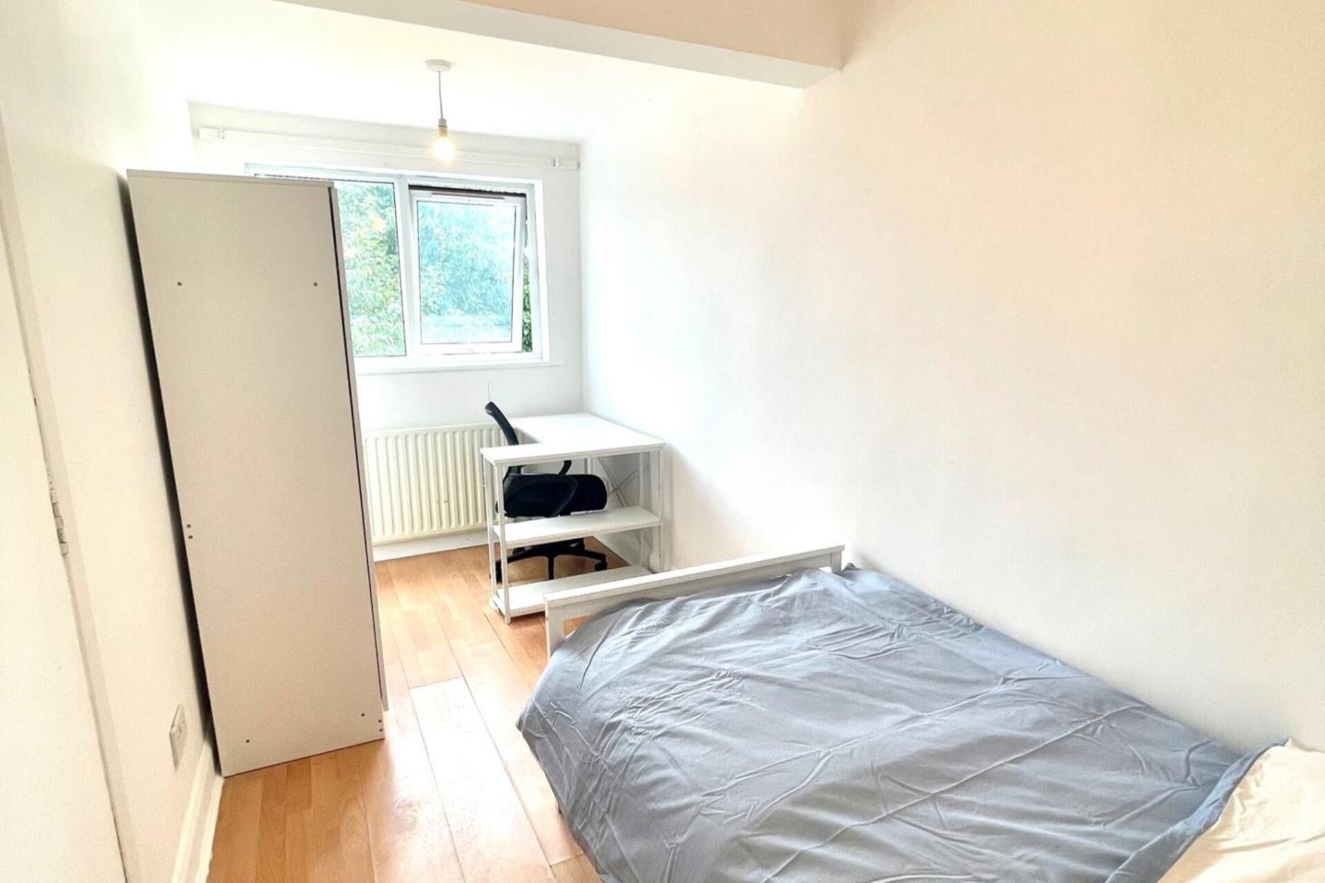 Une petite pièce lumineuse, avec un lit, un bureau et un radiateur.