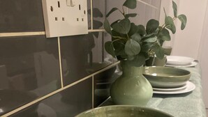 A kitchen with dark tiles, a green vase with leaves, and stacked plates. - Sherwood Hideaway Retreat (Nottingham)