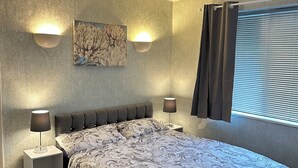 Een slaapkamer met een groot bed, twee bedlampjes, een wandlamp en een raam met zonwering.
