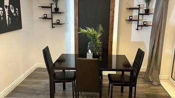 A dining area with a dark wooden table and chairs, a yellow pendant light, and potted plants on shelves.