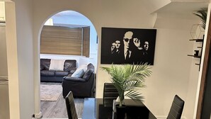 Een eethoek met een zwarte tafel en stoelen, een potplant en een schilderij aan de muur.
