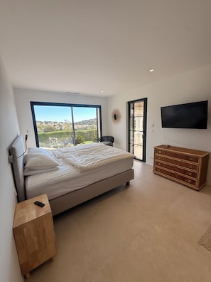 A bedroom with a bed, a TV, a wooden dresser, and a view of a landscape.