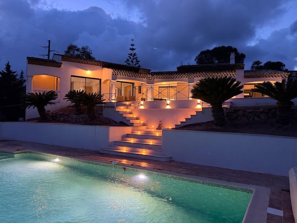 Una casa moderna con piscina, una escalera que conduce al nivel superior e iluminación exterior.