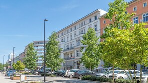 Una hilera de edificios de varios pisos con balcones, coches aparcados y árboles a lo largo de la calle.