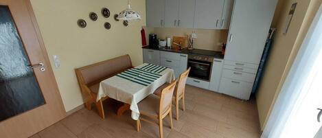 A compact kitchen with a dining table and chairs, a small oven, and cabinets.