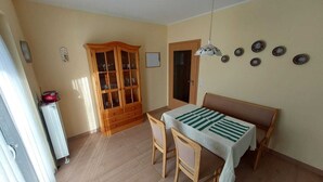 Ruokailutila, jossa on pöytä ja tuolit, lasiovilla varustettu kaappi ja kattotuuletin.