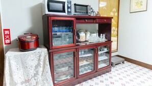A kitchen with a microwave, a rice cooker, and a cabinet with glass doors containing dishes.