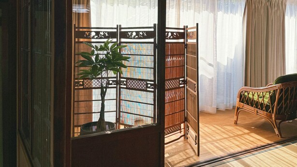 A traditional Japanese room with tatami flooring, a shoji screen, a tatami mat table, a green cushioned chair, and a bamboo plant.