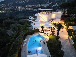 Una villa moderna con piscina, zona de comedor exterior y vistas a la colina circundante.