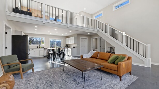 A spacious living area with a high ceiling, a staircase, and a kitchen in the background. - Barndominium w/ Barrel Sauna, Mountain Views, King Bed & Fast WiFi (Berkeley Springs)