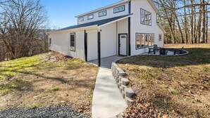 A two-story house with a large front porch, a covered patio, and a stone pathway leading to the entrance. - Barndominium w/ Barrel Sauna, Mountain Views, King Bed & Fast WiFi (Berkeley Springs)