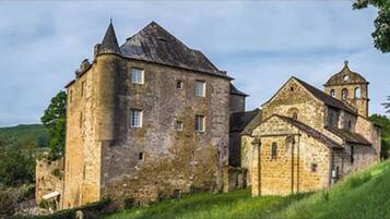 A historic stone building with a prominent tower and a smaller attached structure, likely a church, set in a lush, green landscape.