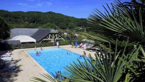 Una piscina con gente alrededor, rodeada de vegetación y edificios.