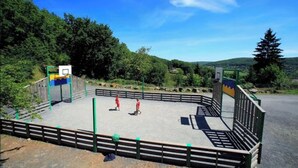 Una cancha de baloncesto al aire libre rodeada por una valla de madera, con dos personas jugando.