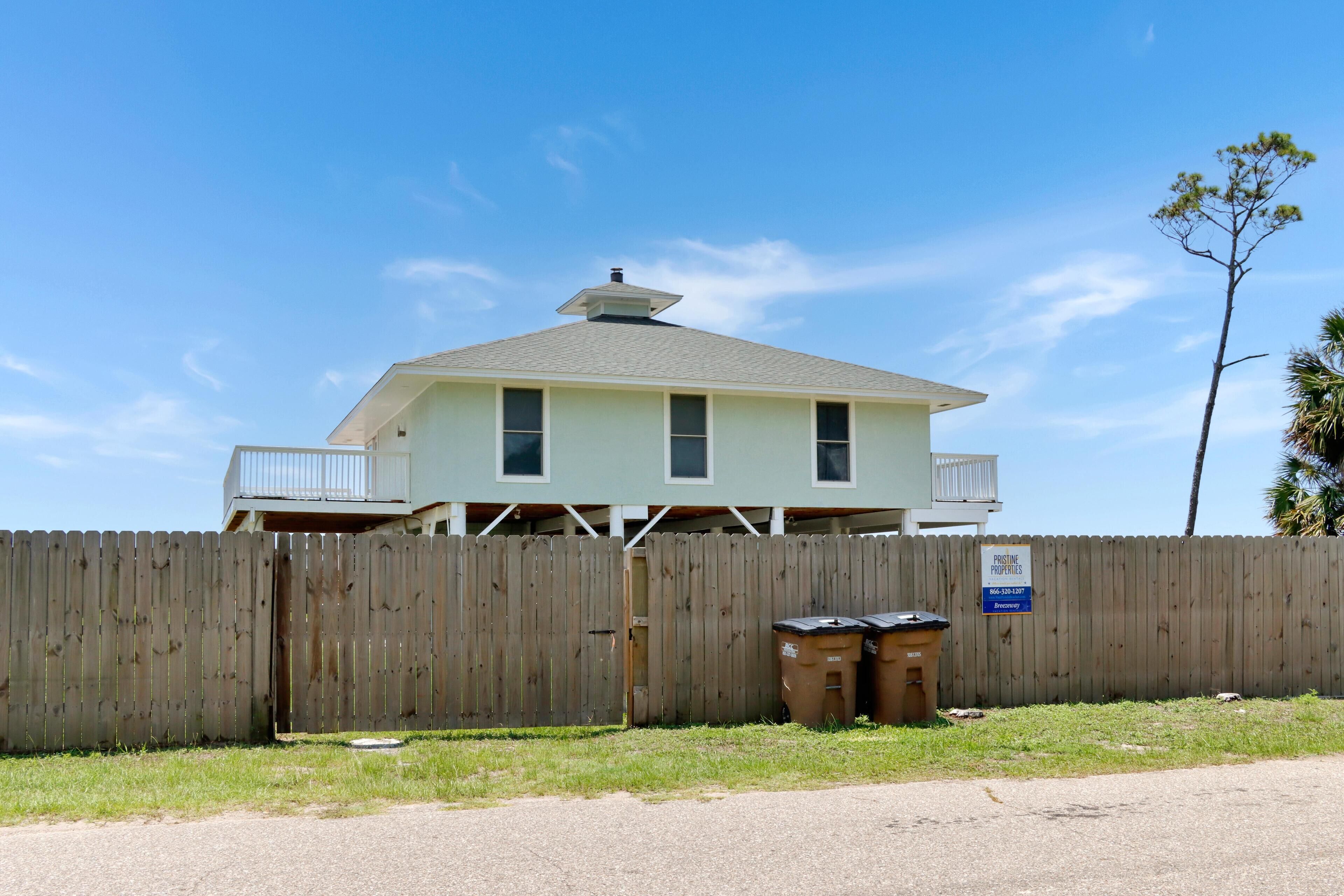 A two-story house with a balcony, a wooden fence, and two trash bins.