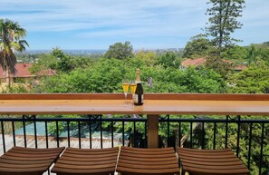 A balcony with a wooden table and chairs, overlooking a lush green landscape and a distant cityscape. - Enjoy Sydney's Northern Beaches. Unique district views, 1950s classic, sleeps 5 (Seaforth)