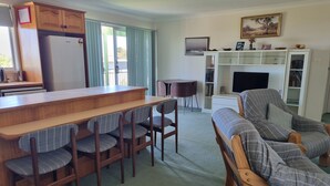 A living room with a wooden bench, a dining table with chairs, a TV, and a bookshelf. - Enjoy Sydney's Northern Beaches. Unique district views, 1950s classic, sleeps 5 (Seaforth)