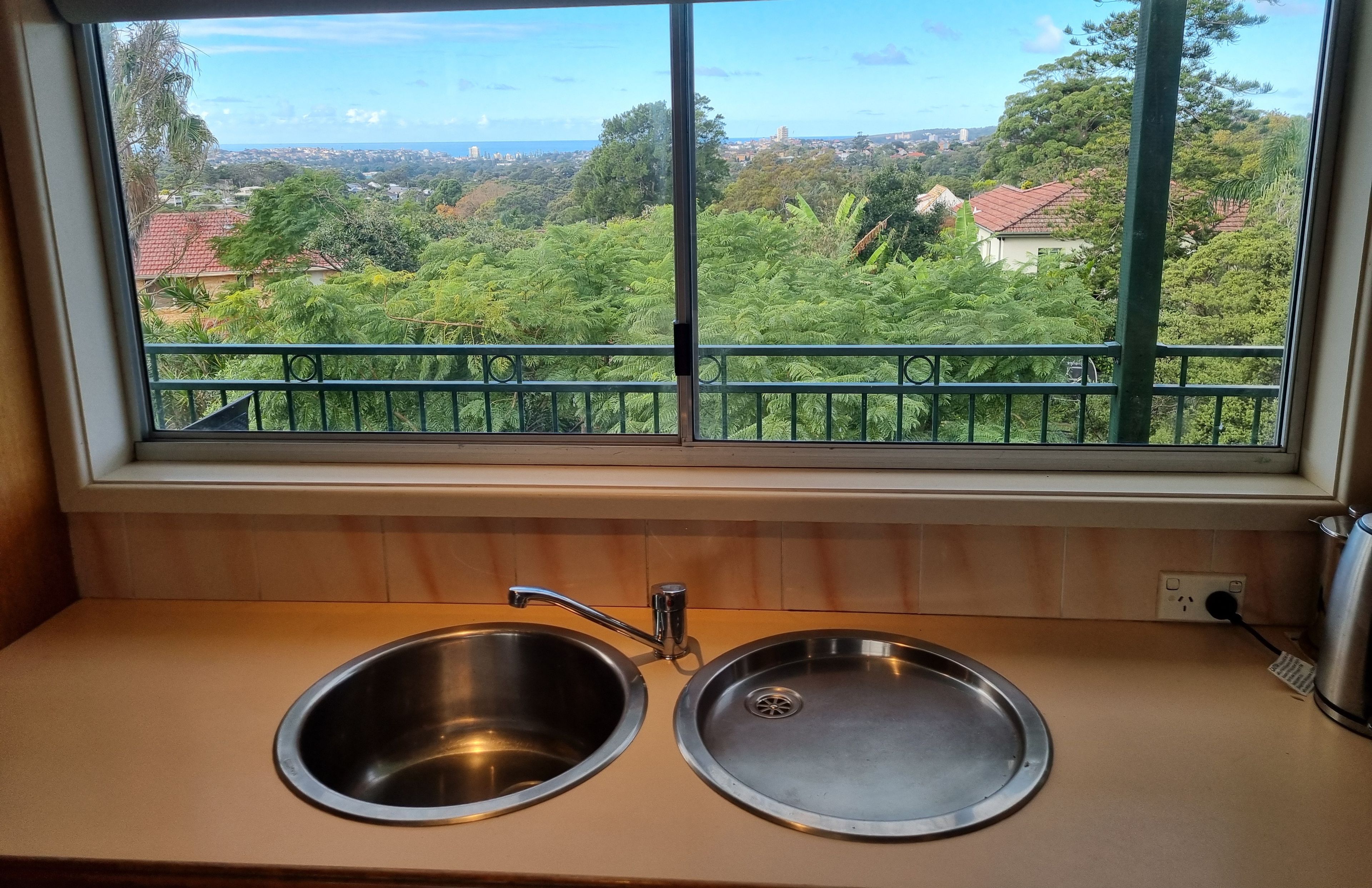 A kitchen with two stainless steel sinks and a window overlooking a green landscape.