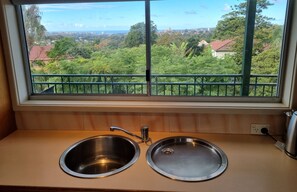 A kitchen with two stainless steel sinks and a window overlooking a green landscape. - Enjoy Sydney's Northern Beaches. Unique district views, 1950s classic, sleeps 5 (Seaforth)