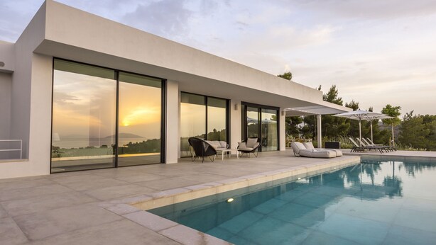 A modern house with a swimming pool, large glass windows, and outdoor seating.