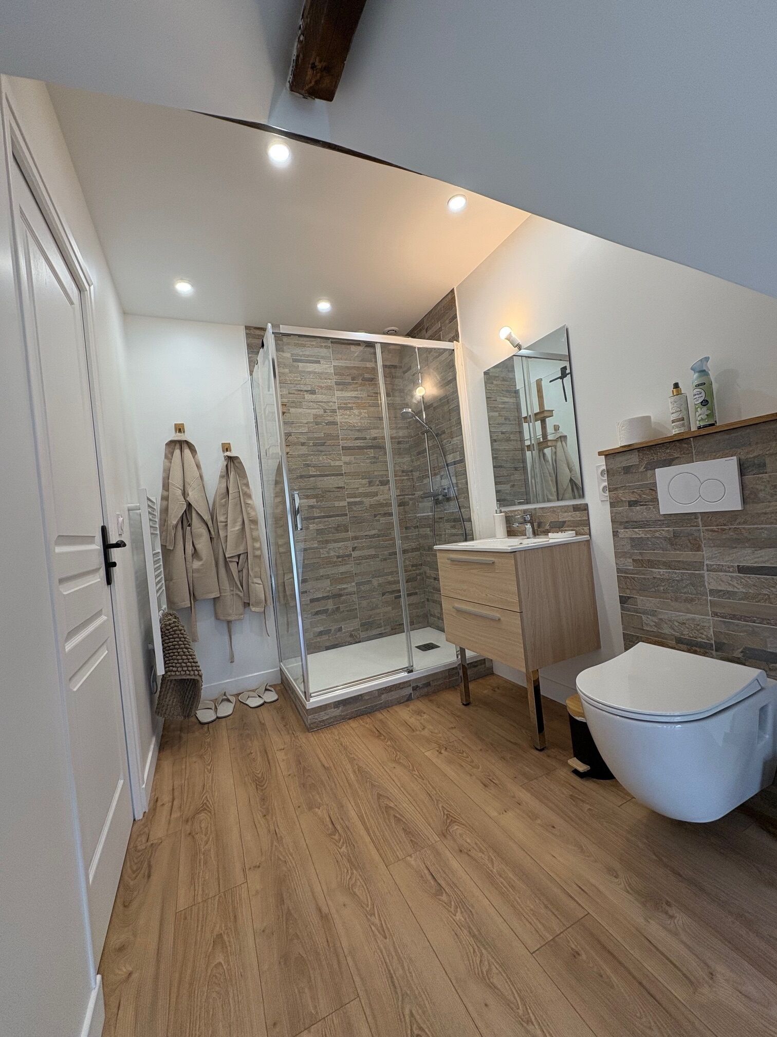 A modern bathroom with a glass shower, wooden flooring, a white toilet, and a vanity with a mirror.