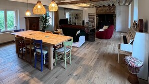A spacious living area with a wooden dining table, chairs, a red sofa, a piano, and a djembe drum.