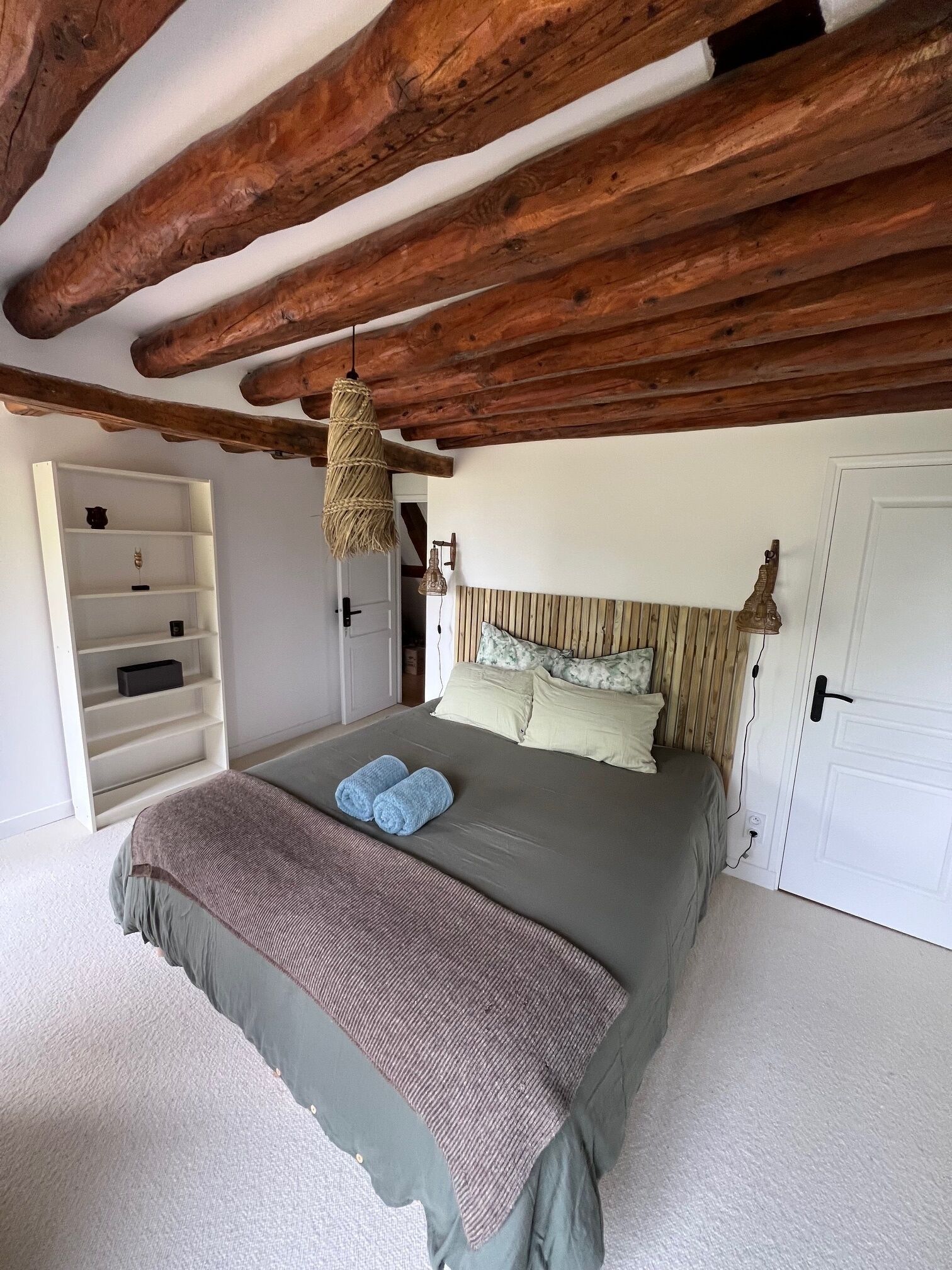 A bedroom with a bed, a wooden ceiling, a white wardrobe, and a hanging light fixture.