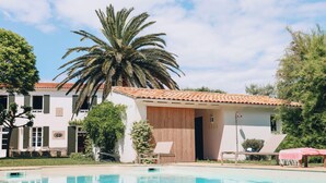 A poolside area with a palm tree, a building with a tiled roof, and a covered seating area. - Villa Phoenix - Ancient and modern charm (La Couarde sur mer)